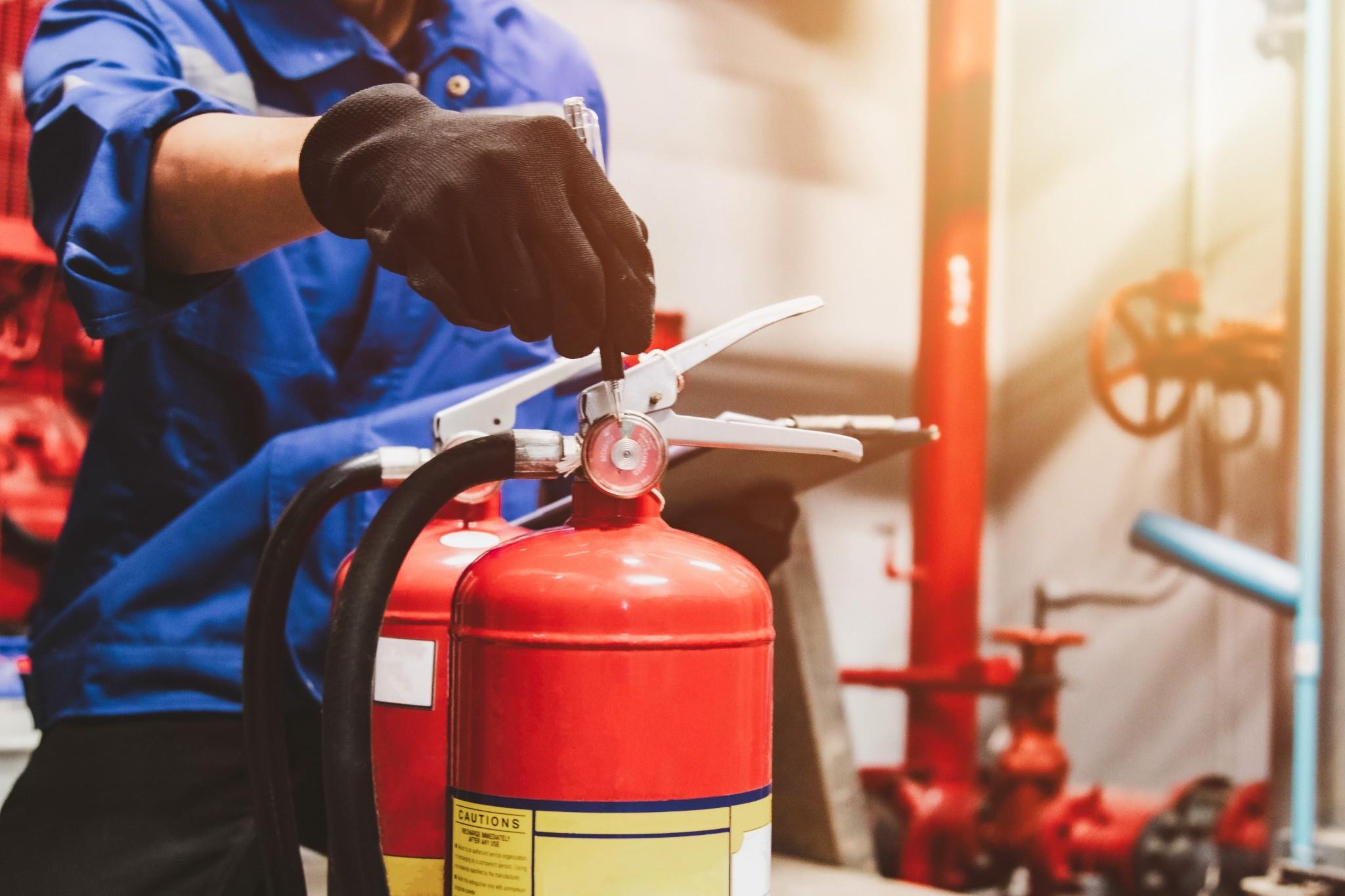 Technician inspecting and servicing a commercial fire extinguisher in a mechanical room